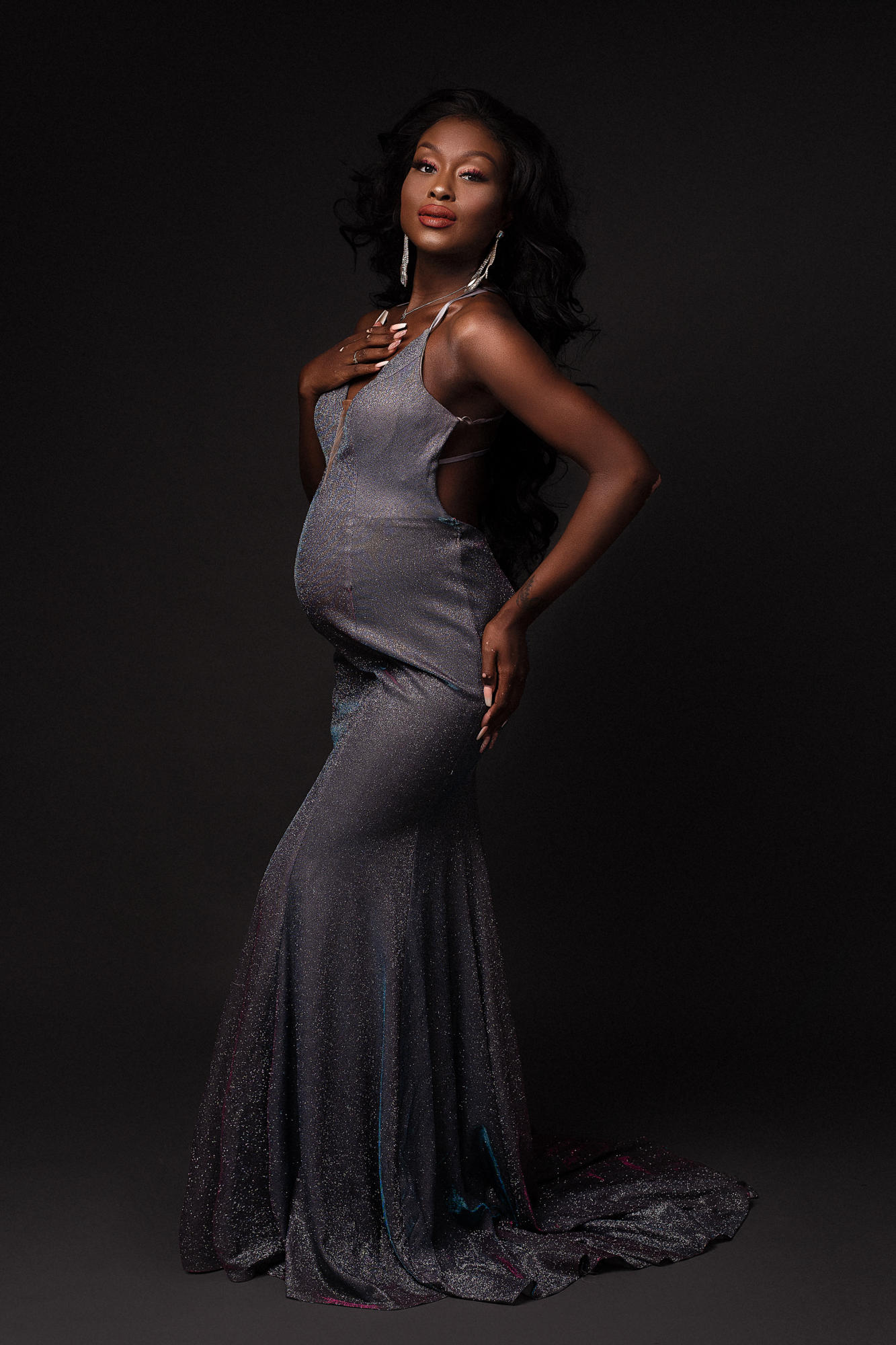 Pregnant Woman Posing with her hand resting on her chest and her other on her back. Wearing a ball gown